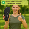 Lächelnde Frau im Grünen zeigt die Sohle eines Barfußschuhs mit flexibler Struktur und hebt den Daumen – Text im Bild: Dünne und flexible Sohle, bereit für jede Situation