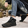 Schwarze Barfuß-Winterschuhe mit Kontrastnähten und warmem Futter, getragen von einer Person in Jeans und schwarzer Jacke auf einem Holzweg in herbstlicher Umgebung.