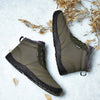Grüne Barfuß-Winterschuhe mit schwarzer Profilsohle, warmem Innenfutter und seitlichem „FASHION“-Label, flach fotografiert auf winterlichem Hintergrund mit getrocknetem Laub.