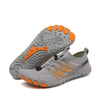 Graue Barfußschuhe mit Orangenen Details und zehenförmiger Profilsohle. Ein Schuh liegt flach, der andere zeigt die flexible Sohle mit rutschfestem Profil
